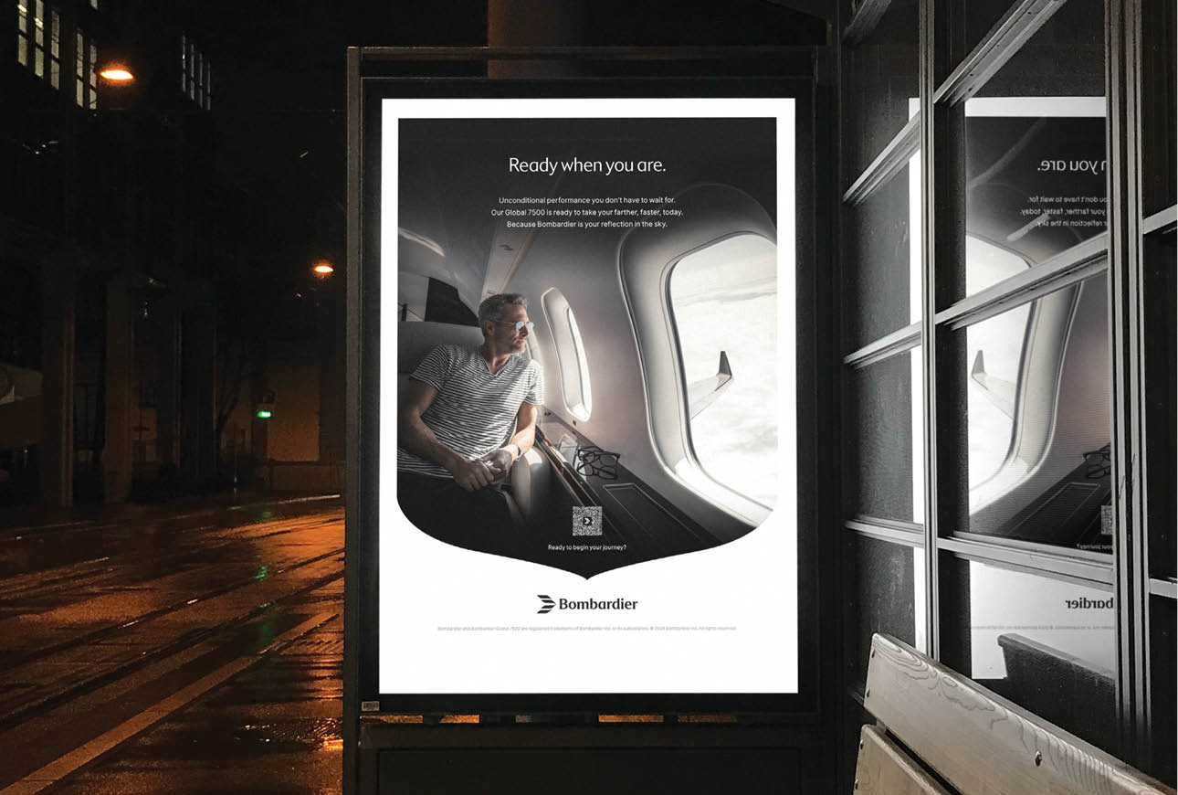 Illuminated outdoor advertisement displaying Bombardier private jet interior imagery.