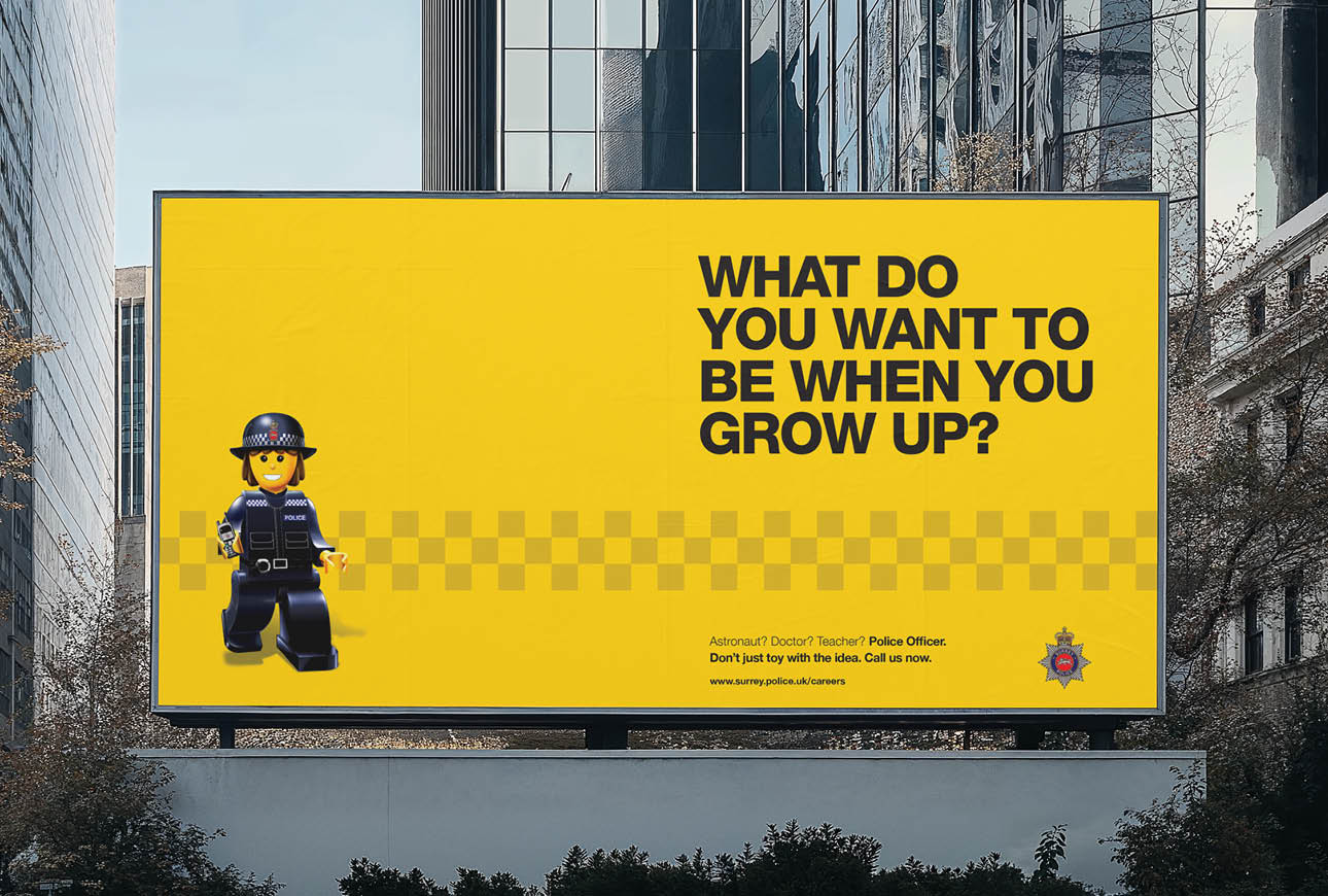 Surrey Police recruitment billboard with yellow background and toy police officer in urban city setting